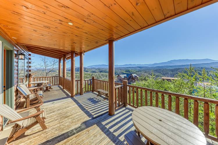 Outdoor furniture on an under cover back deck to a large cabin with a beautiful mountain view
